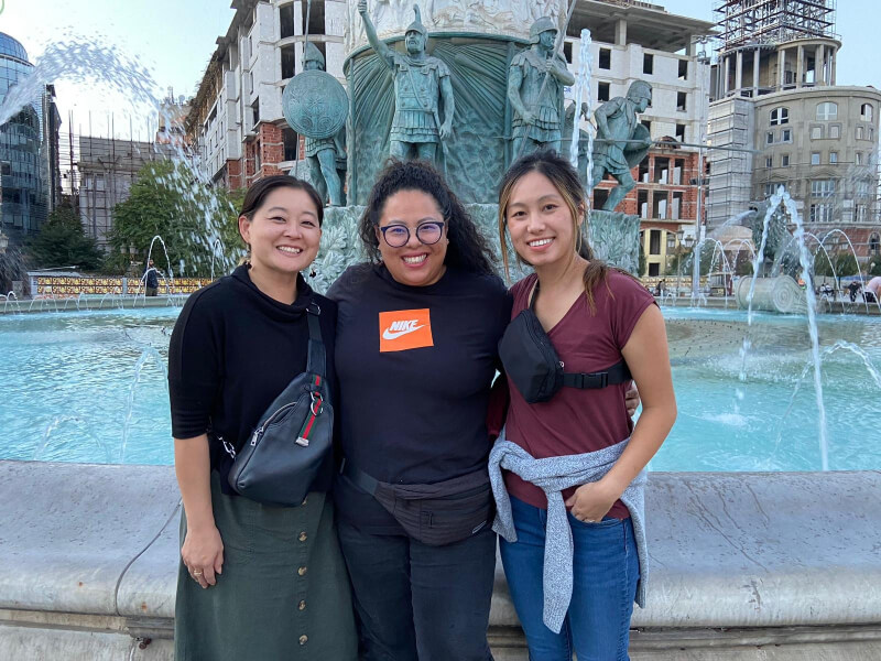 Three women and behind them is a fountain with Roman soldier statues
