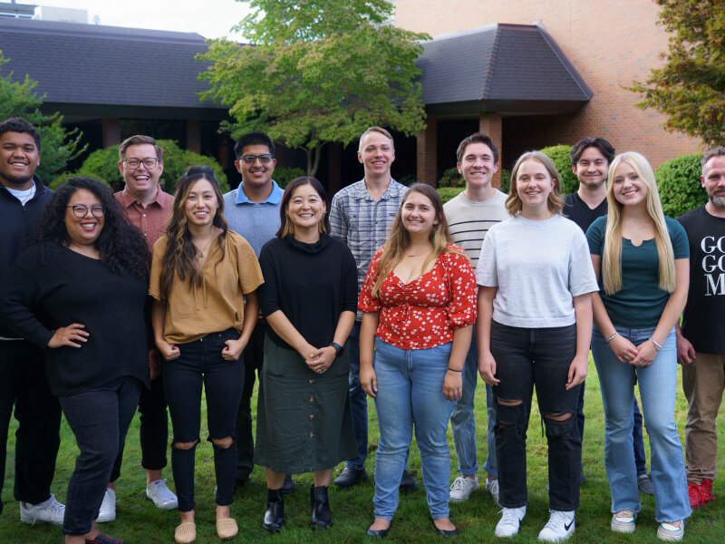 A group of people standing on green grass in front of a brick building