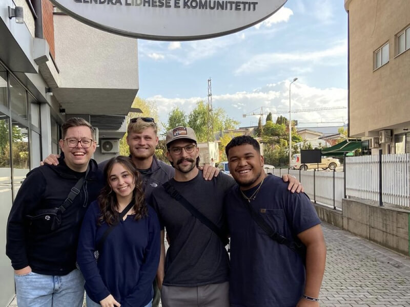5 people on a sidewalk with their arms around each other's backs